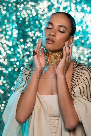 brunette african american woman in shawl and gold on neck posing with closed eyes on sparkling blue background 