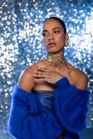 Elegante afrikanisch-amerikanische Frau in blauem Pullover und Folie am Hals auf glitzerndem Hintergrund 