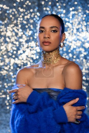 Fashionable african american woman with golden foil on neck looking at camera on sparkling background 