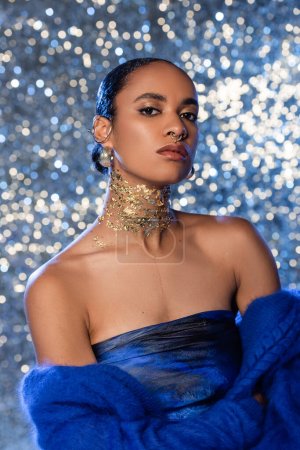 Trendy african american model in soft blue sweater and golden foil on neck on sparkling background 