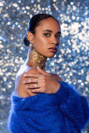 Modische afrikanisch-amerikanische Frau in blauem Pullover und Accessoires auf glitzerndem Hintergrund 