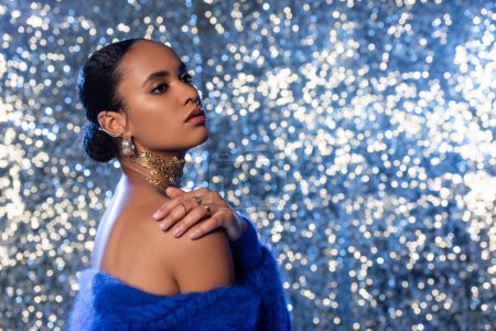 Photo for Young african american woman with foil on neck and accessories touching shoulder on sparkling background - Royalty Free Image