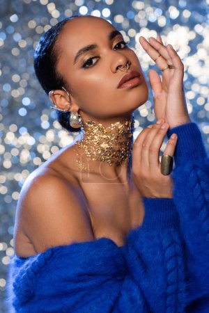 Fashionable african american woman in blue faux fur jacket and golden accessories on sparkling background 