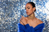 Pretty african american woman with foil on neck touching bare shoulder on sparkling background  puzzle #620709022