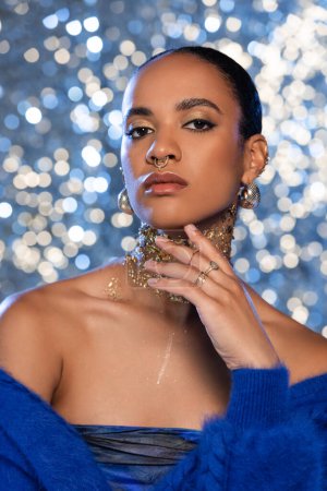 Portrait of trendy african american woman with makeup and golden foil on neck posing on sparkling background 
