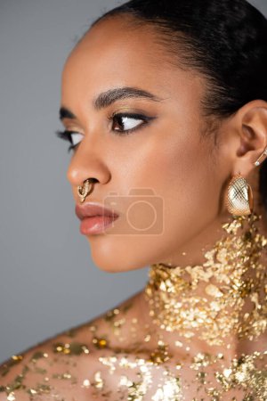 Retrato de joven modelo afroamericano con lámina dorada en el cuello mirando hacia otro lado aislado en gris 