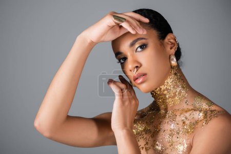 Fashionable african american woman with foil on neck and chest posing isolated on grey 