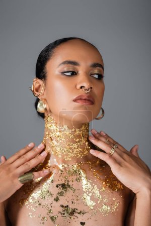 Elegantes afrikanisch-amerikanisches Modell mit goldener Folie auf der Brust, die den Hals berührt, isoliert auf grau 