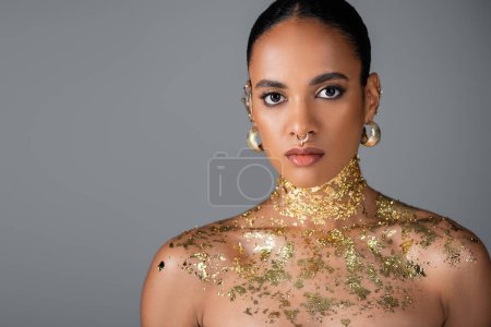 Afroamerikanisches Modell mit goldenen Accessoires und Folie auf der Brust isoliert auf grau 