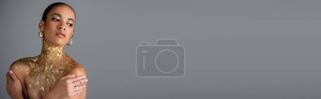 Photo for African american model with foil on chest touching shoulders isolated on grey with copy space, banner - Royalty Free Image
