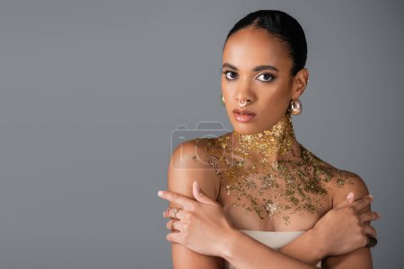 Pretty and stylish african american model with golden foil on neck isolated on grey 