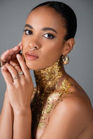 Portrait de modèle afro-américain élégant avec accessoires et feuille d'or sur la poitrine isolée sur gris 