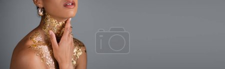 Cropped view of african american woman touching golden foil on neck and chest isolated on grey, banner 