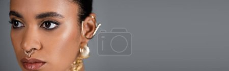 Close up view of young african american woman with golden piercing isolated on grey, banner 