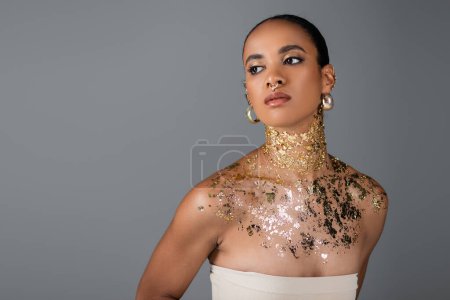Téléchargez les photos : Jeune femme afro-américaine avec feuille sur le cou et piercing doré isolé sur gris - en image libre de droit