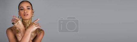Téléchargez les photos : Modèle afro-américain à la mode avec feuille d'or sur le corps regardant la caméra isolée sur gris, bannière - en image libre de droit