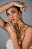 Trendy african american woman with accessories and golden foil on body and hands posing isolated on grey  Poster #620709586