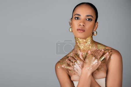 Téléchargez les photos : Femme afro-américaine à la mode avec une feuille d'or sur le cou et les mains en regardant la caméra isolée sur gris - en image libre de droit