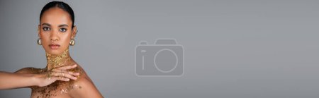 Téléchargez les photos : Jeune modèle afro-américain avec feuille sur le corps et accessoires dorés isolés sur gris avec espace de copie, bannière - en image libre de droit