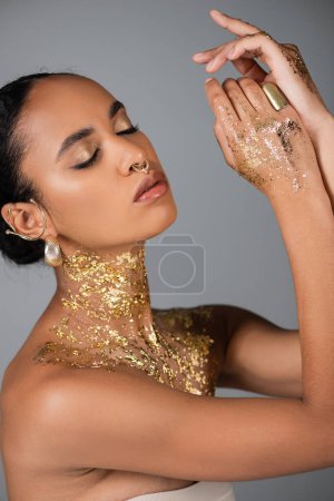 Hübsche afrikanisch-amerikanische Frau mit goldener Folie auf dem Körper posiert isoliert auf grau 