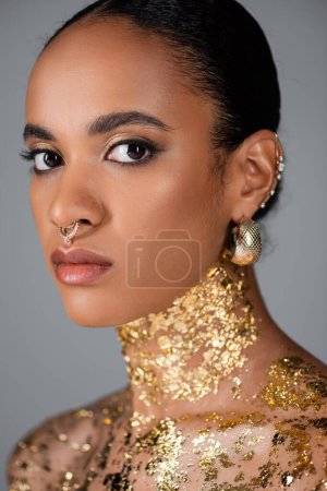 Young african american woman with accessories and foil on chest isolated on grey 