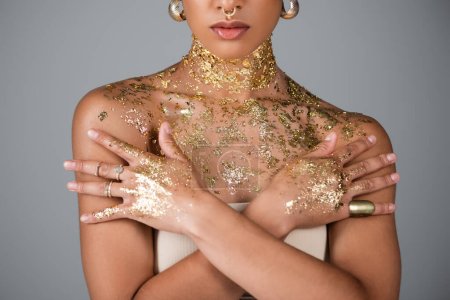Teilansicht des afrikanisch-amerikanischen Modells mit goldener Folie an Händen und Brust, die isoliert auf grau posiert 