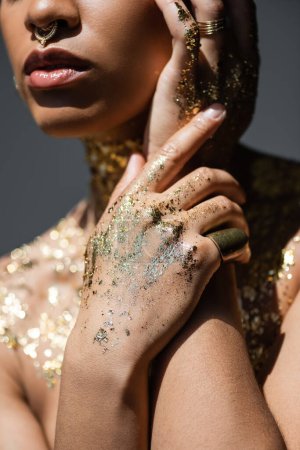 Téléchargez les photos : Vue recadrée du modèle afro-américain tendance avec feuille d'or sur les mains et le corps isolé sur gris avec de la lumière - en image libre de droit