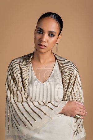 Pretty african american woman in shawl looking at camera isolated on beige 