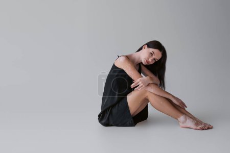 Pretty brunette woman with vitiligo in satin dress looking at camera on grey background