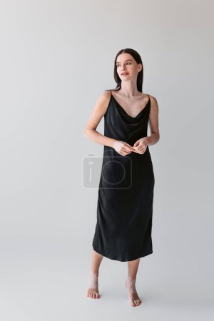 Smiling woman with vitiligo in camisole dress standing on grey background 