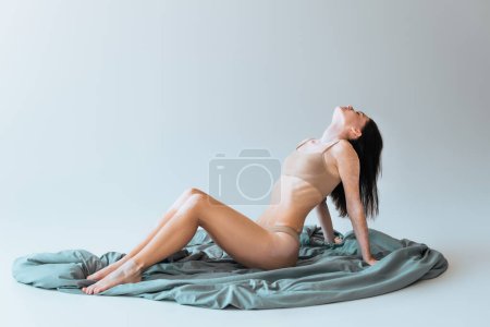 young woman with vitiligo chronical skin condition sitting on blanket and posing on grey 