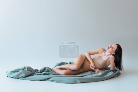 brunette woman with vitiligo skin condition and closed eyes lying on blanket on grey background 