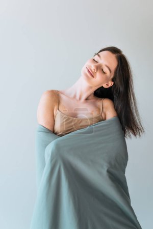 mujer alegre con condición de la piel vitiligo de pie cubierta de manta aislada en gris 