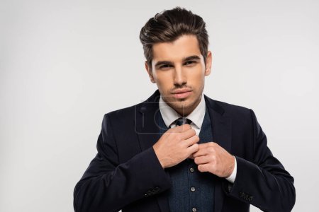 Foto de Hombre de negocios guapo y joven en traje ajustando corbata aislado en gris - Imagen libre de derechos