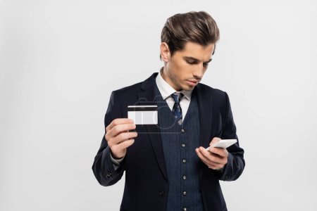 homme d'affaires en costume utilisant smartphone et tenant la carte de crédit isolée sur gris