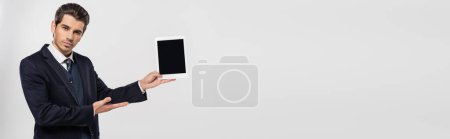 jeune homme d'affaires en costume tenant tablette numérique avec écran blanc isolé sur gris, bannière