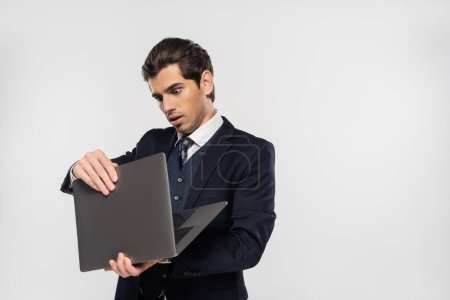 Photo for Shocked businessman in suit looking at laptop isolated on grey - Royalty Free Image