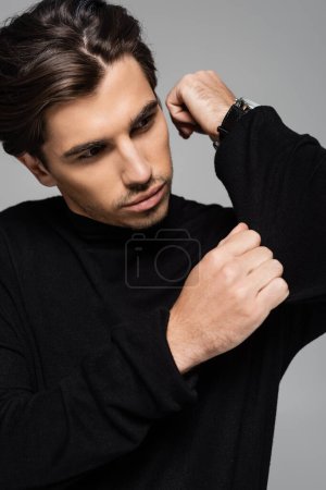 portrait of good looking man in black turtleneck looking away isolated on grey