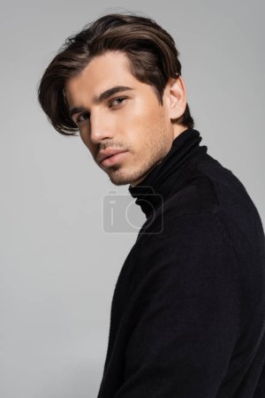 portrait of good looking man posing in black turtleneck isolated on gray