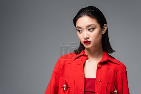 portrait of brunette asian woman in red fashionable jacket isolated on grey