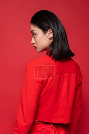 young asian woman in trendy blazer and ear cuff looking away isolated on red