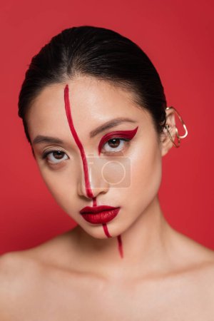Téléchargez les photos : Portrait de femme asiatique avec manchette élégante et visage artistique regardant la caméra isolée sur rouge - en image libre de droit