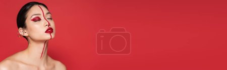 Téléchargez les photos : Jeune femme asiatique avec les épaules nues et le maquillage artistique posant avec les yeux fermés isolé sur rouge, bannière - en image libre de droit