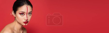 Téléchargez les photos : Jeune asiatique femme avec créatif visage et oreille poignets regarder caméra isolé sur rouge, bannière - en image libre de droit