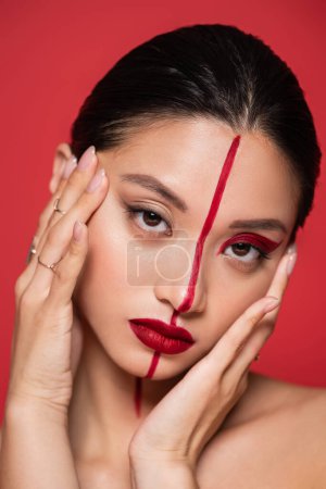 Porträt einer asiatischen Frau, die Gesicht mit perfekter Haut und künstlerischem Aussehen berührt, isoliert auf Rot