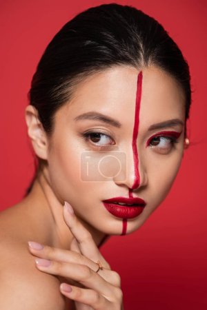 Téléchargez les photos : Portrait de femme asiatique avec visage artistique lumineux regardant loin isolé sur rouge - en image libre de droit