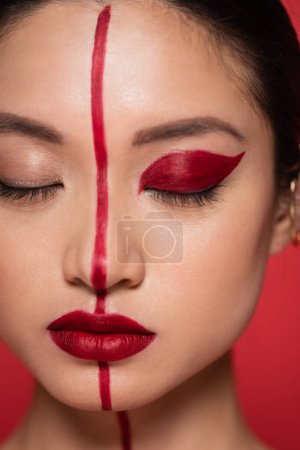 close up portrait of asian woman with closed eyes and creative makeup isolated on red