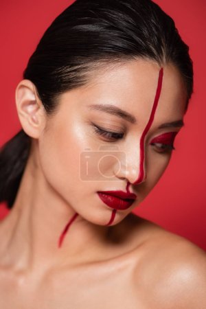 Téléchargez les photos : Portrait de brunette asiatique femme avec visage créatif et épaule nue posant isolé sur rouge - en image libre de droit