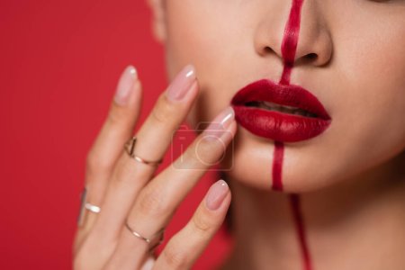 vista parcial de la mujer tocando los labios brillantes en la cara dividida con la línea aislada en rojo