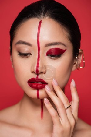 portrait of young asian woman artistic makeup and ear cuff touching face isolated on red